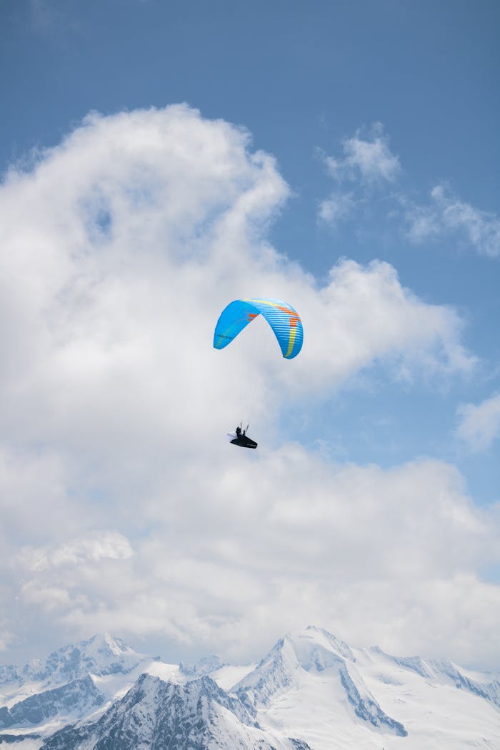 Paraglider flying high above the snowy Alps with a bright blue sky backdrop.